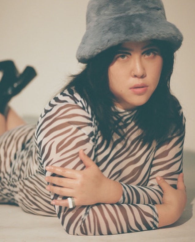 Jin Baek posing for model photoshoot wearing a russian hat and camouflauge body con dress
